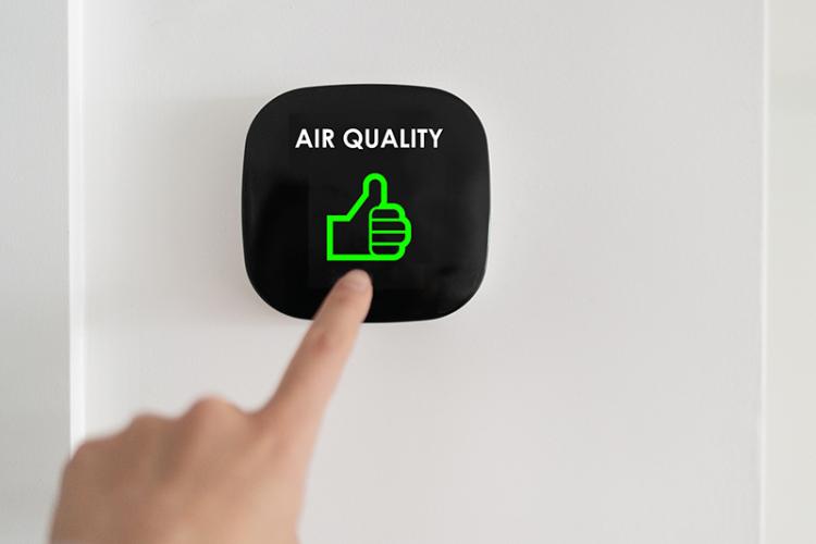 Person touching programmable thermostat with a screen displaying "Air quality" and a thumbs up symbol.